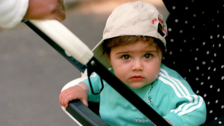 Lourdes Leon in a stroller as a baby wearing a baseball cap and sweatshirt