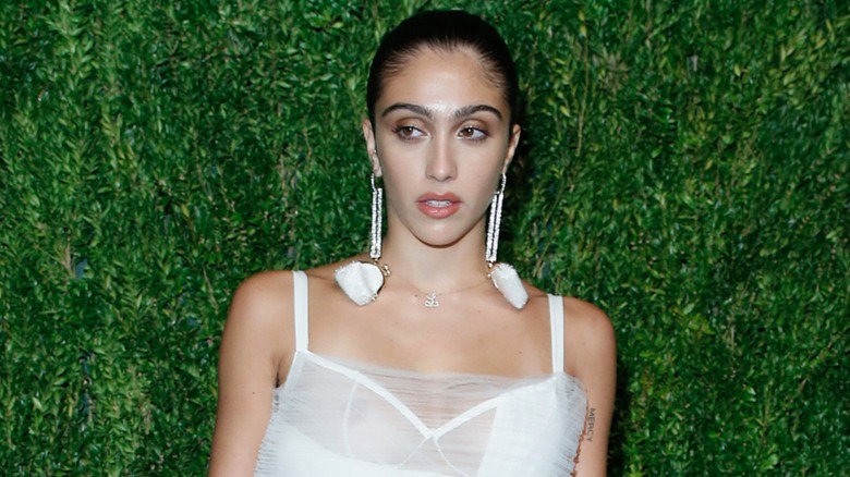 Lourdes Leon posing in a white mini dress in 2018 in front of a green foliage background
