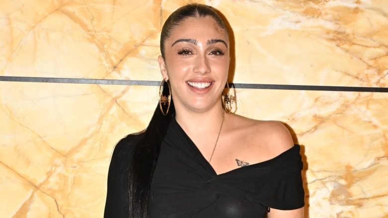 Lourdes Leon posing in front of an orange marble wall in a short black dress at Paris Fashion Week 2023