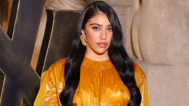 Lourdes Leon posing in a shiny, mustard color dress with her long, dark hair down