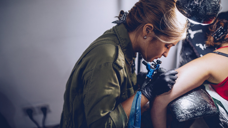 woman tattooing a woman's arm at tattoo studio