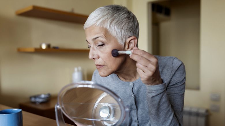 Older woman applying makeup in a mirror