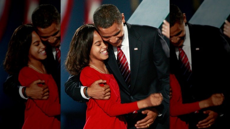 Malia Obama, with loosely curled hair, smiling and embracing her father on election night