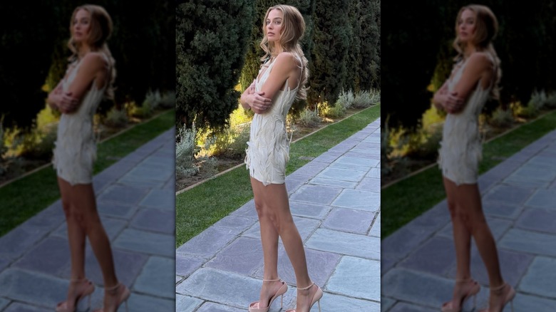 Margot Robbie on a garden path in a white tank dress covered with feathers