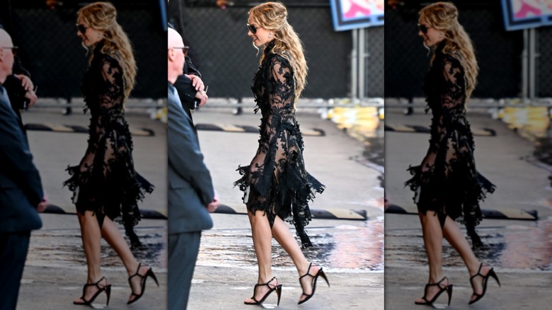 Margot Robbie walking on the street in a black lace dress and heel