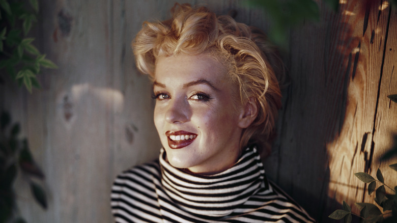 Marilyn Monroe smiling into the camera while wearing a striped shirt and her classic red lip