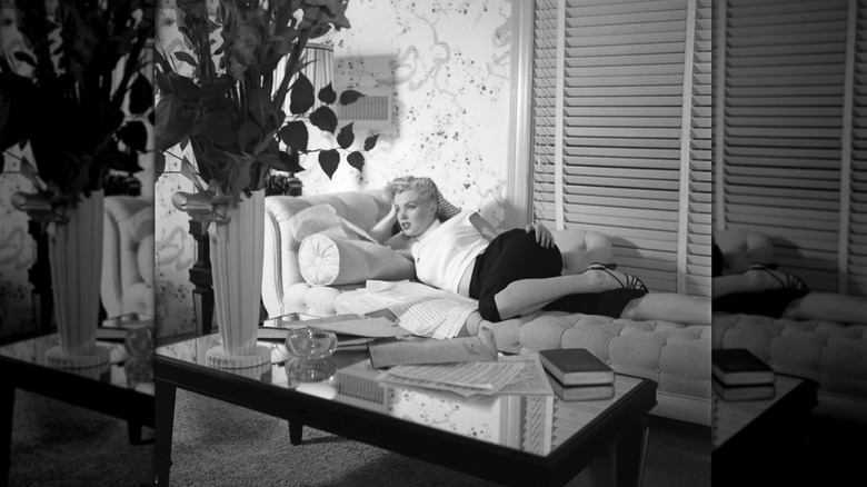 Marilyn Monroe lounging on a couch while wearing a white top, black pants, and heels