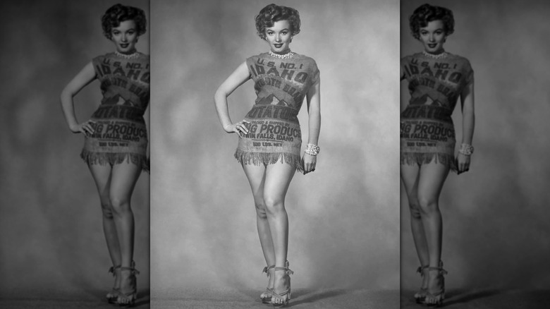 Marilyn Monroe grinning into the camera while posing in a potato sack dress