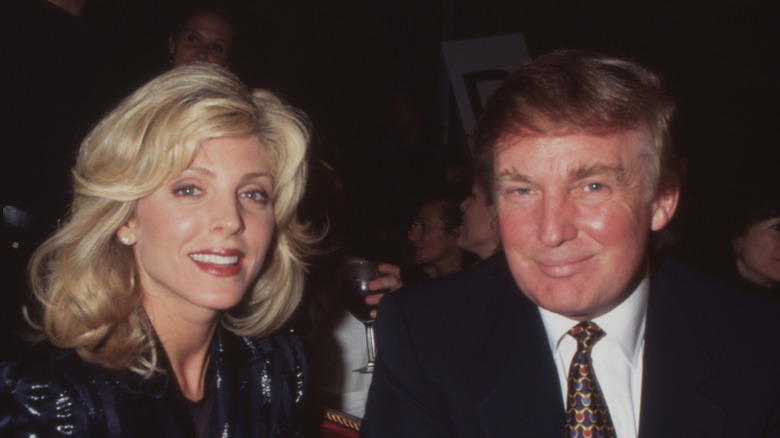 Marla Maples wears big gold earings and a shirt next to Donald Trump scowling in a suit