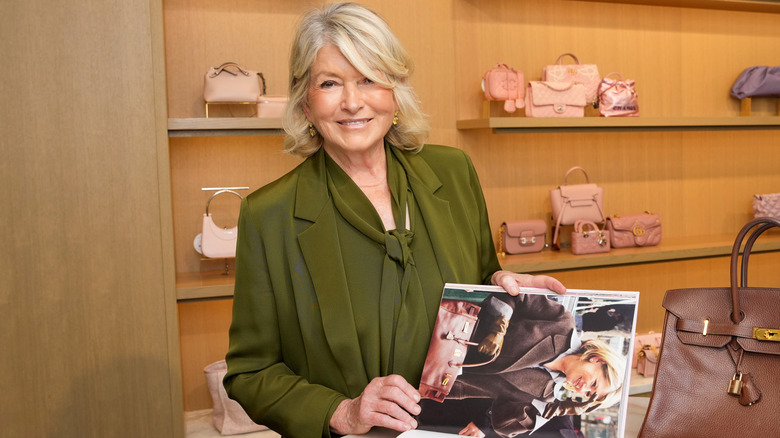 Martha Stewart in olive green holding a book showing her nails