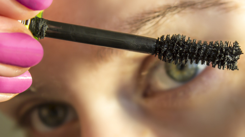 Woman with green eyes holding mascara wand