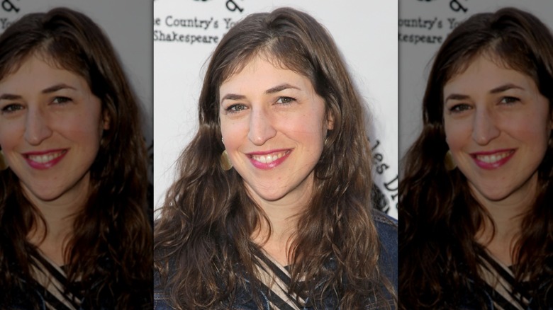 Mayim Bialik wearing a pink lipstick and pre grey brunette hair