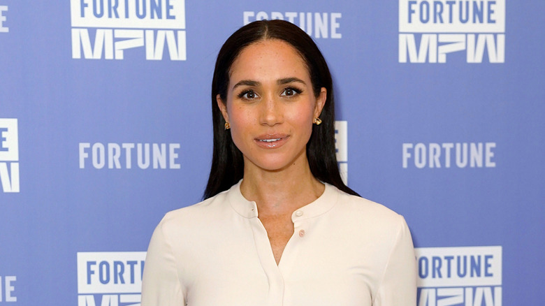 Meghan Markle on the red carpet with straight hair and wearing a white shirt dress