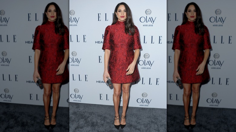 Meghan Markle posing on the red carpet in 2014 in a patterned, dark red mini dress