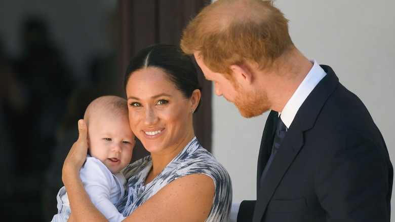 Meghan Markle smiling and holding her son while Prince Harry looks at her in 2019