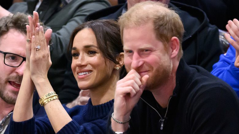 Meghan Markle and Prince Harry seated at a sports game and smiling