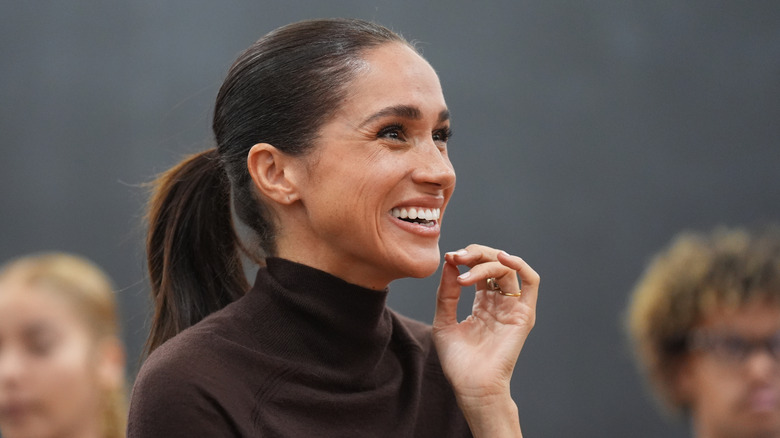 Meghan Markle smiling and touching her face