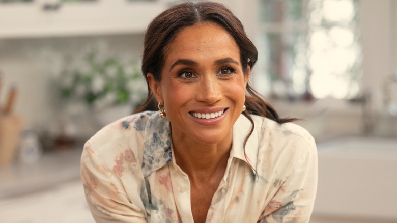 Meghan Markle smiling while leaning on a surface in her Netflix show