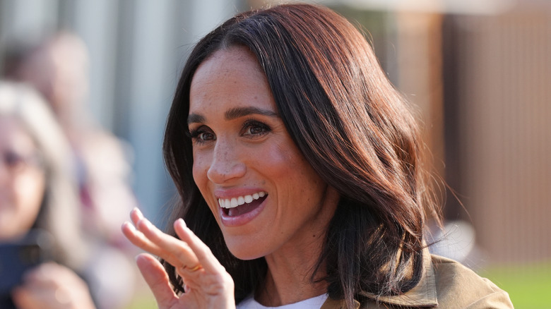 A close up of Meghan Markle waving at people in an olive green jacket