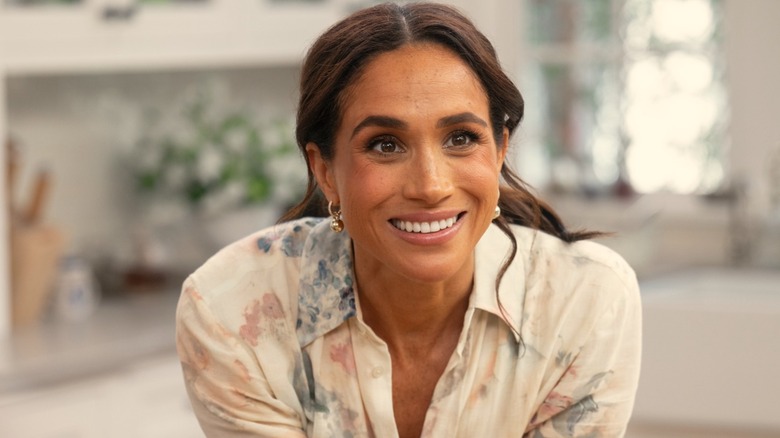 Meghan Markle smiling while leaning on a surface in her Netflix show