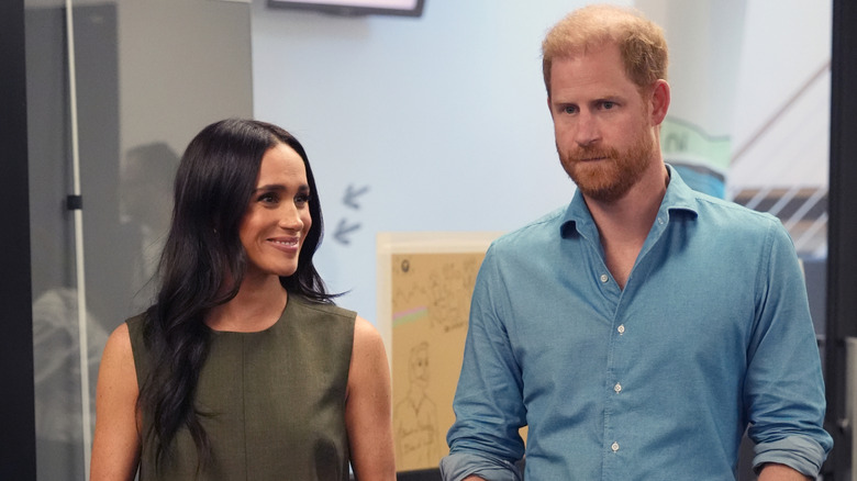 Prince Harry and Meghan Markle at an event, with Meghan smiling and Harry looking neutral