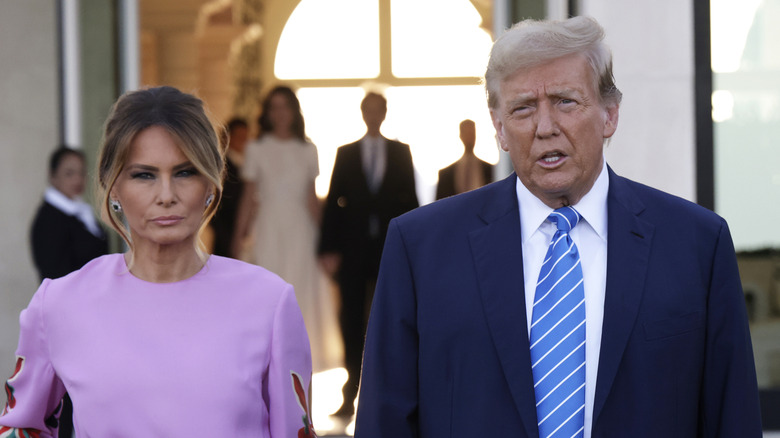 Melania Trump in purple while Donald Trump walks beside her in a suit