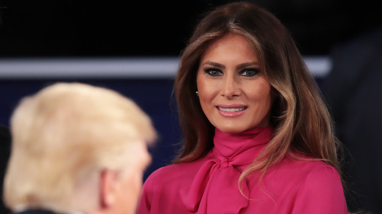Melania Trump in a pink blouse smiling at Donald Trump at a debate in 2016