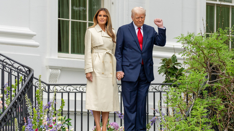 Melania Trump standing next to Donald Trump in a beige trench coat