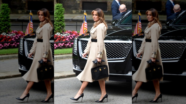 Melania Trump walking in front of an SUV in a shirt dress with a black purse
