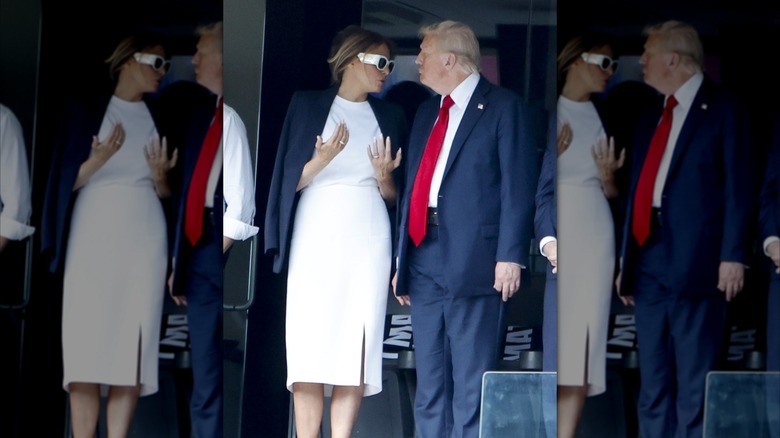 Melania Trump standing next to Donald Trump in a white outfit with a navy jacket