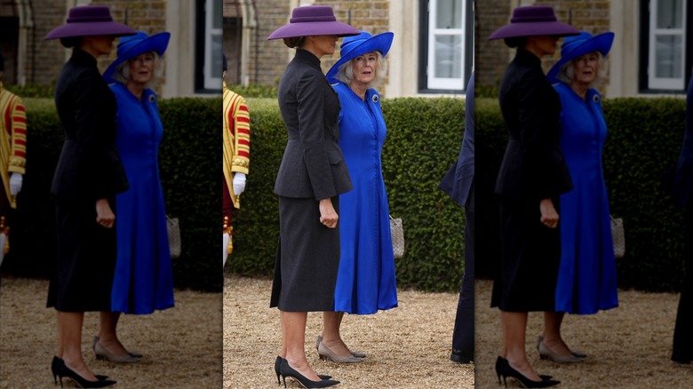 Melania Trump wearing a suit and large hat and standing next to Queen Camilla