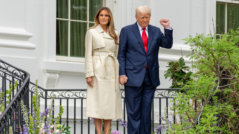 Melania Trump standing on an exterior White House staircase in a trench coat with Donald Trump