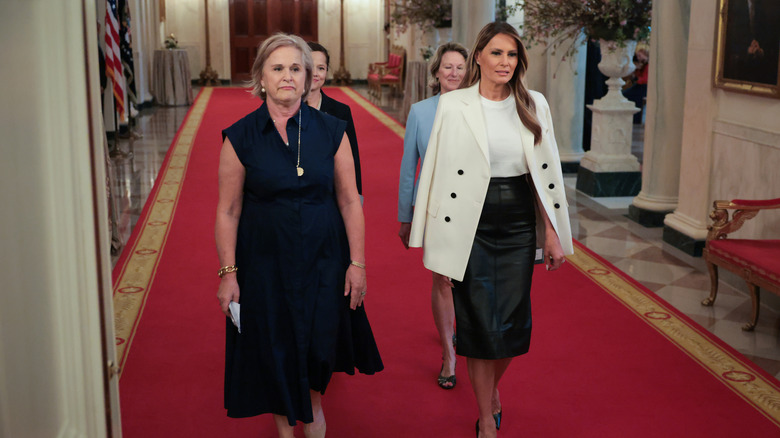 Melania Trump walking down a hallway with three other women and wearing black and white