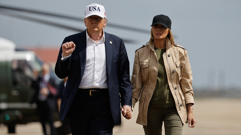 Melania Trump walking alongside Donald Trump while wearing a black cap