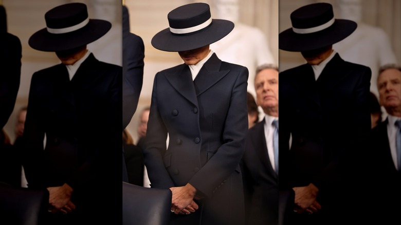Melania Trump wearing a suit and large hat and looking downward