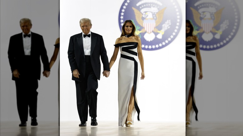Melania Trump walking alongside Donald Trump and wearing a white and black gown