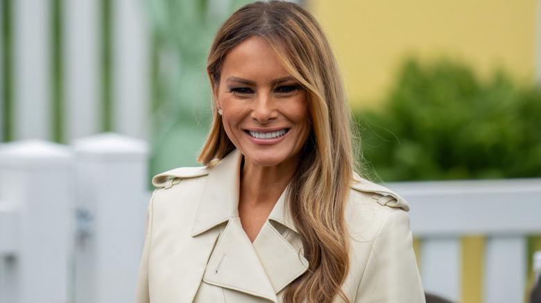 Melania Trump smiling in a trench coat