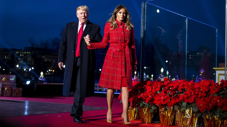 Donald Trump holding Melania Trump's hand while she wears a red coat