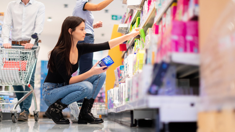Woman crouches down at store while shopping for menstrual hygiene products