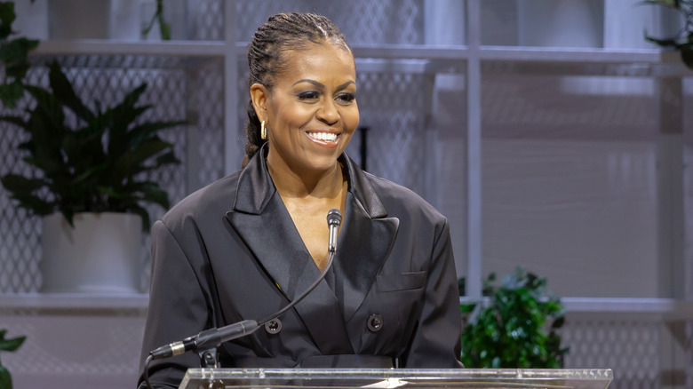 Michelle Obama on stage in 2023 smiling at the audience wearing a black jacket