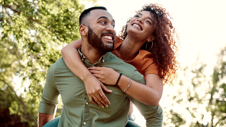 A couple having fun outside as the man gives a woman a piggyback ride