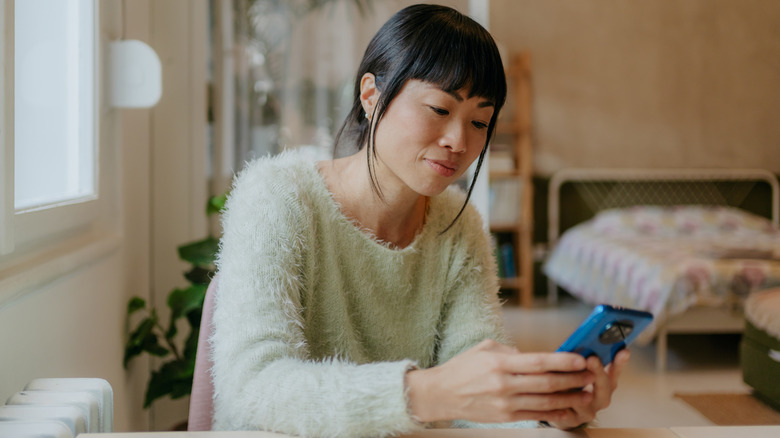 Woman in a fuzzy sweater focusing on her blue smart phone while at home
