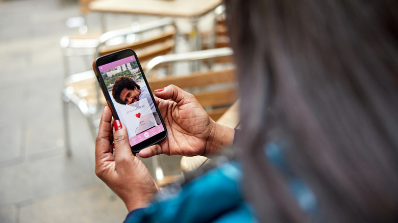 Unseen woman holding phone with a dating app open and a potential suitor on screen
