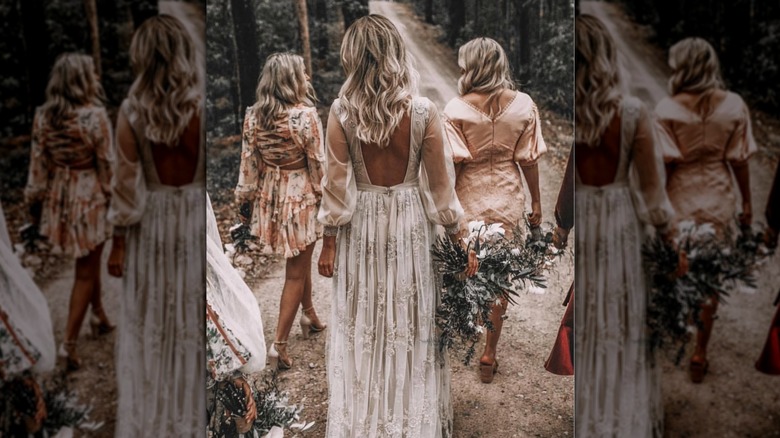 A boho bride with her back to the camera walking with bridesmaids in the woods