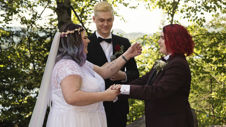 Young brides holding hands while smiling in front of an officiant
