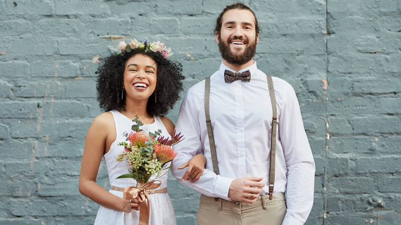 Bride and groom posing against blue bricks, with the bride wearing a flower crown while groom sports suspenders and a bowtie