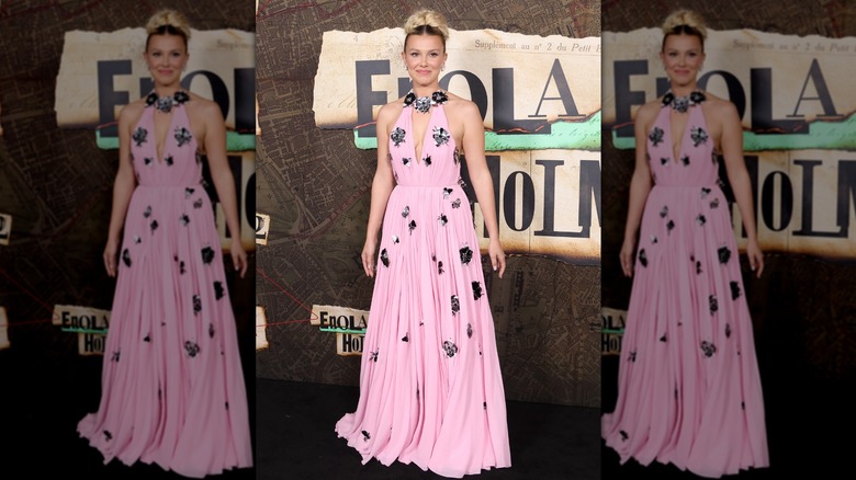 Millie Bobby Brown posing with in a pink, halter-style dress embellished with black and white flowers at a premiere