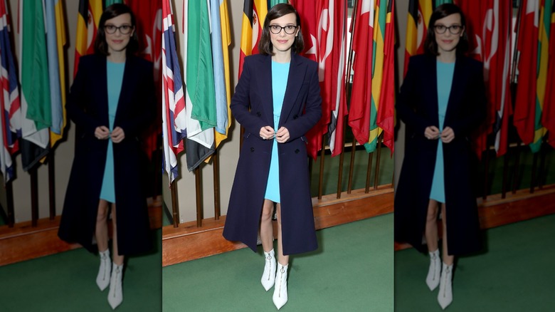 Millie Bobby Brown wearing a bright blue dress under a navy trench coat at a UNICEF event