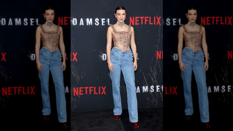 Millie Bobby Brown posing at a Damesel event in a corset-style top and jeans