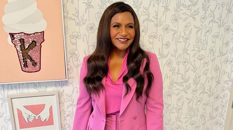 Mindy Kaling smiling and posing in a pink suit and top in 2021